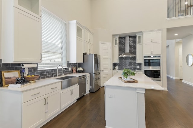 kitchen with wall chimney range hood, stainless steel appliances, sink, a center island, and white cabinetry