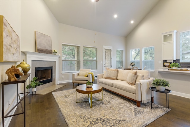 living room with a tiled fireplace, high vaulted ceiling, and dark wood-type flooring