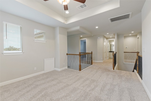 spare room featuring light colored carpet, a raised ceiling, and ceiling fan