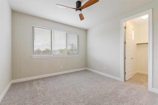 unfurnished bedroom featuring ceiling fan, a walk in closet, a closet, and light colored carpet