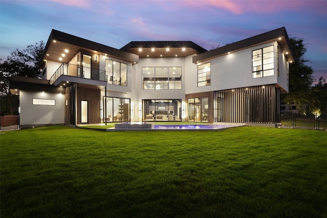 back house at dusk featuring a balcony and a lawn