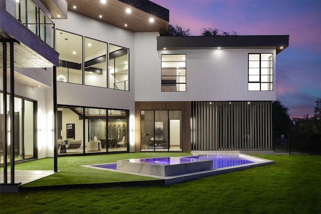 back house at dusk with an in ground hot tub and a lawn