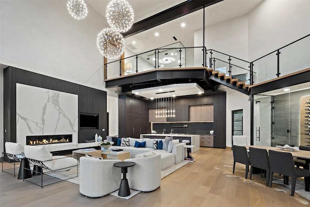 living room featuring a towering ceiling, a premium fireplace, light hardwood / wood-style floors, and a notable chandelier