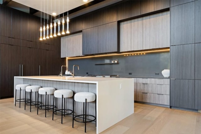 300 Stonewall Ln, Austin, TX 78746 - kitchen featuring modern cabinets, light wood-style flooring, a breakfast bar area, a kitchen island with sink, and light countertops