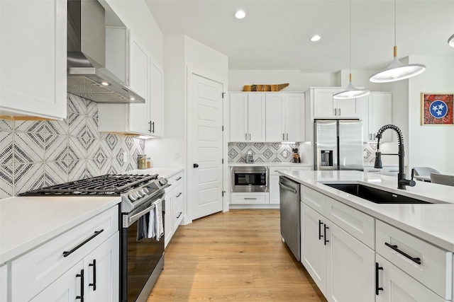 kitchen featuring a sink, stainless steel appliances, light countertops, wall chimney exhaust hood, and light wood-type flooring