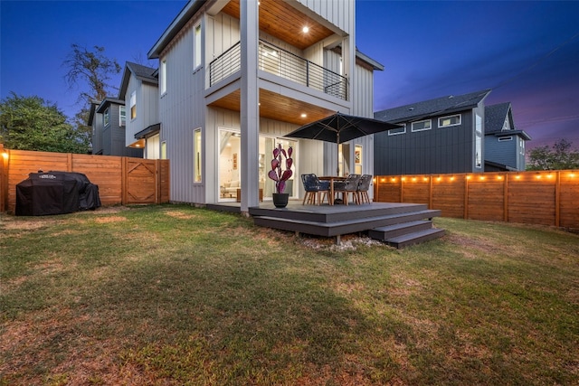 back of house with a fenced backyard, a yard, board and batten siding, and a balcony