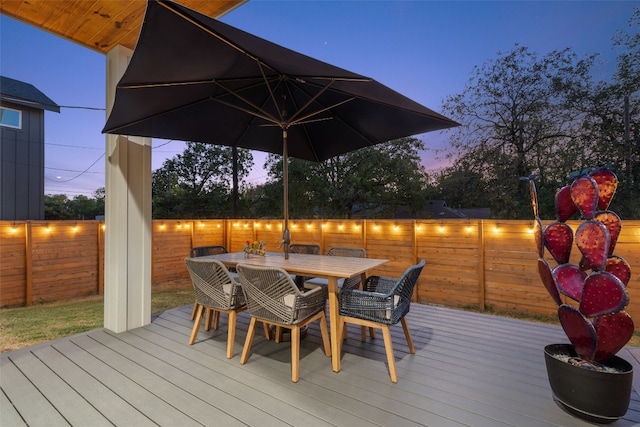 deck at dusk featuring outdoor dining area and fence