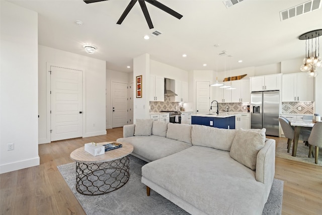 living room with visible vents, light wood-style floors, and a ceiling fan