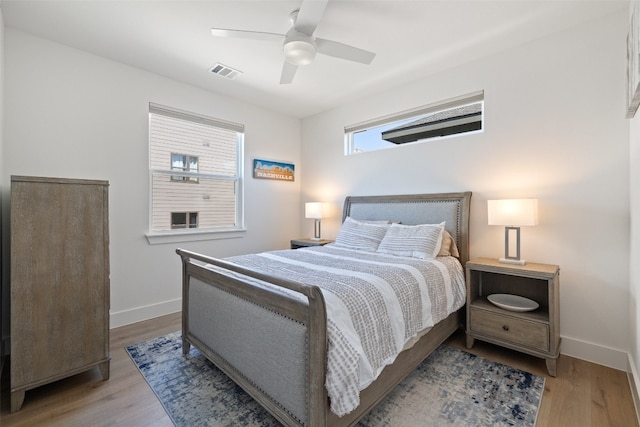 bedroom with a ceiling fan, wood finished floors, visible vents, and baseboards