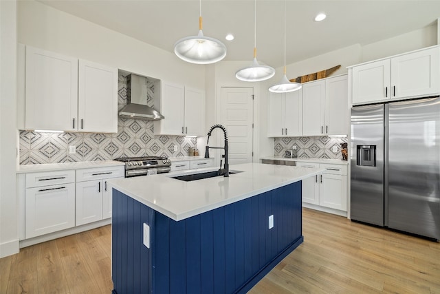 kitchen featuring a sink, stainless steel appliances, light countertops, wall chimney range hood, and light wood-type flooring