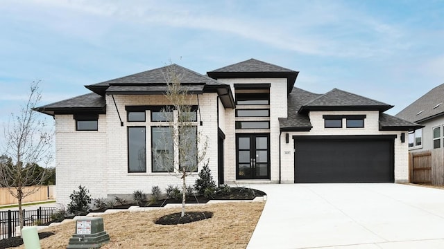 prairie-style home featuring a garage, concrete driveway, brick siding, and fence