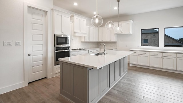 kitchen featuring stainless steel appliances, light countertops, a kitchen island with sink, a sink, and white cabinetry