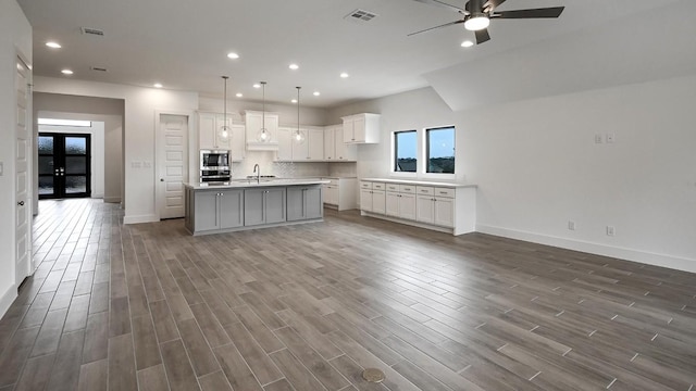 kitchen with light countertops, hanging light fixtures, visible vents, white cabinets, and an island with sink