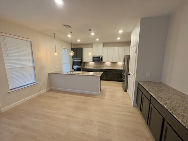 kitchen with white cabinets, hanging light fixtures, light stone countertops, light wood-type flooring, and stainless steel appliances