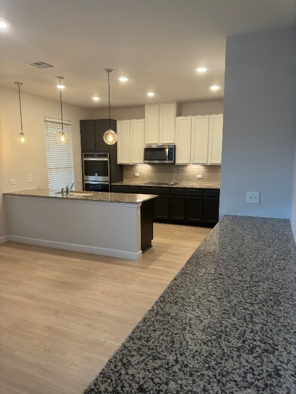 kitchen with white cabinetry, backsplash, stainless steel appliances, and light hardwood / wood-style flooring