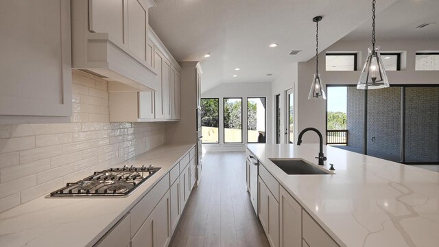 kitchen featuring appliances with stainless steel finishes, a sink, backsplash, and light stone countertops