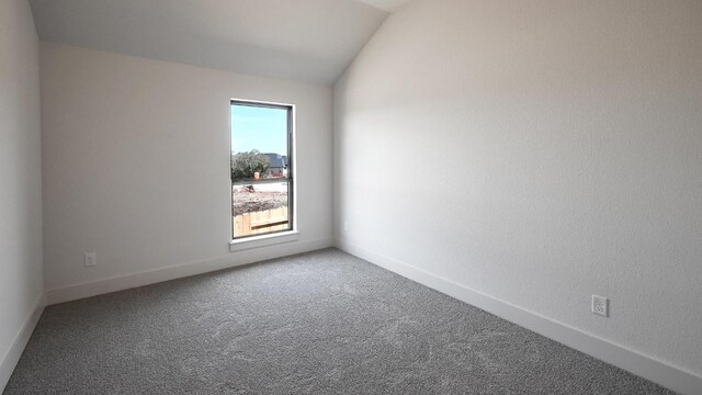 carpeted spare room featuring lofted ceiling and baseboards