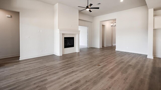 unfurnished living room featuring a tile fireplace, ceiling fan with notable chandelier, wood finished floors, visible vents, and baseboards