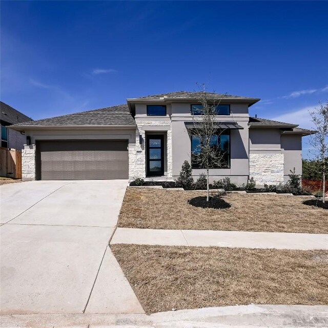 prairie-style house featuring a garage, stone siding, driveway, and stucco siding