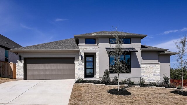 prairie-style home with an attached garage, fence, stone siding, concrete driveway, and stucco siding