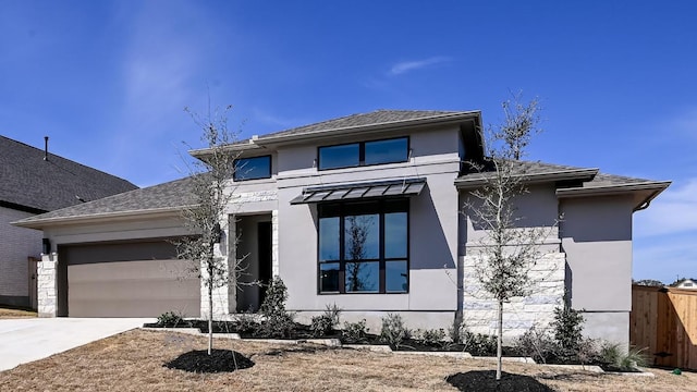 prairie-style house with a garage, fence, driveway, roof with shingles, and stucco siding