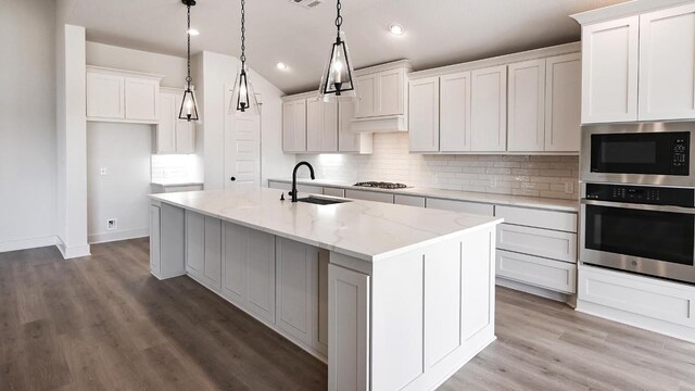 kitchen with a center island with sink, stainless steel appliances, backsplash, a sink, and wood finished floors