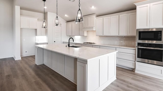 920 Teakmill Trl, San Marcos, TX 78666 - kitchen with appliances with stainless steel finishes, a sink, tasteful backsplash, an island with sink, and light wood-type flooring