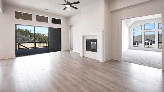 unfurnished living room featuring a high ceiling, ceiling fan, a tiled fireplace, and wood finished floors