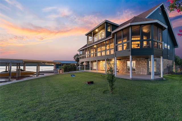 back house at dusk featuring a patio area, a yard, and a sunroom