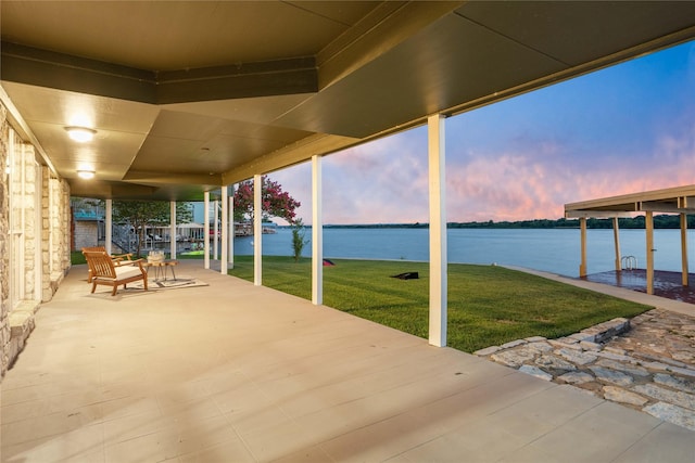 patio terrace at dusk featuring a water view and a yard