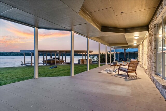 patio terrace at dusk featuring a water view and a yard