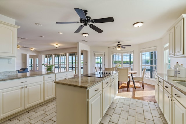 kitchen featuring stone countertops, black electric stovetop, kitchen peninsula, and a healthy amount of sunlight