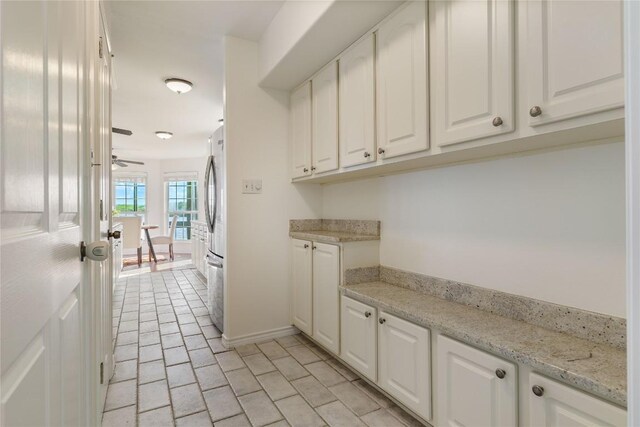 kitchen featuring light stone counters, stainless steel fridge, and white cabinets