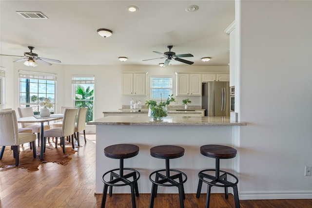 kitchen with white cabinetry, kitchen peninsula, stainless steel fridge, a wealth of natural light, and light stone counters