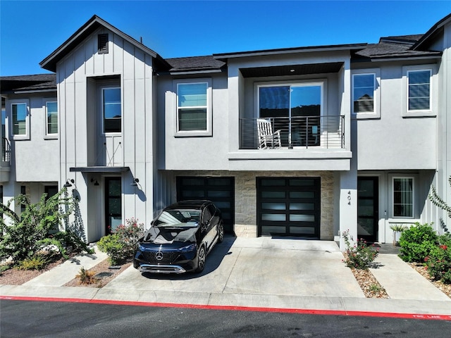 view of property featuring a balcony, driveway, stone siding, board and batten siding, and an attached garage