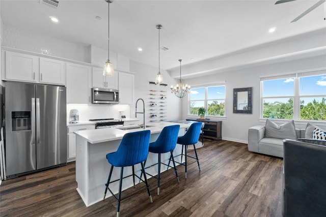 kitchen with white cabinets, a center island with sink, dark hardwood / wood-style flooring, decorative light fixtures, and stainless steel appliances