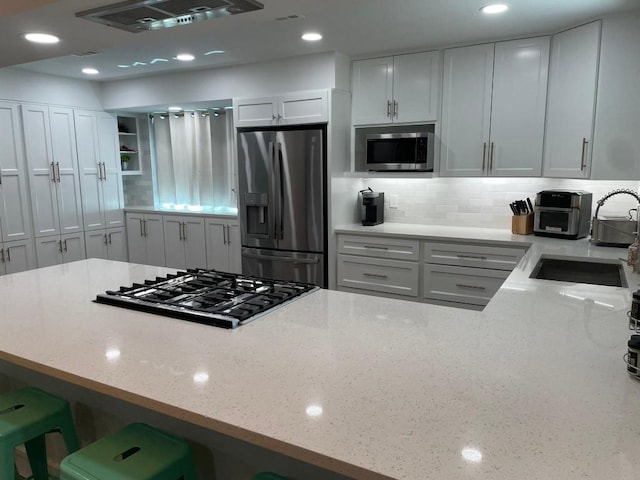 12404 Sceptre Cv, Austin, TX 78727 - kitchen featuring appliances with stainless steel finishes, light stone countertops, range hood, decorative backsplash, and a breakfast bar