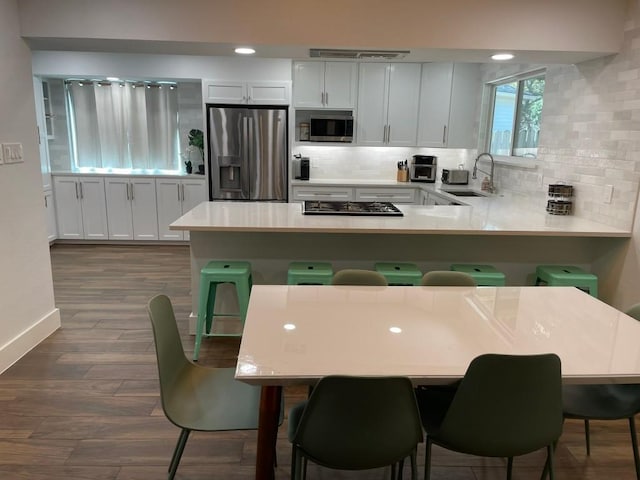 12404 Sceptre Cv, Austin, TX 78727 - kitchen featuring appliances with stainless steel finishes, decorative backsplash, a peninsula, light countertops, and dark wood finished floors