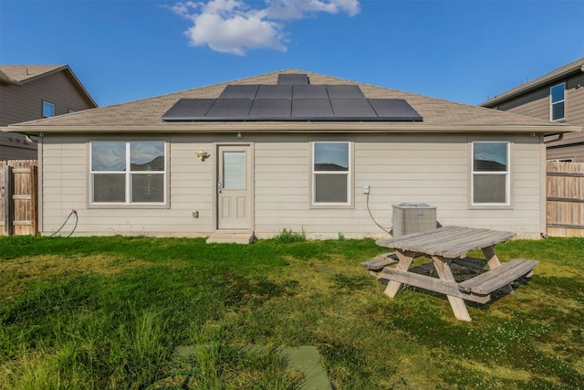 rear view of house featuring solar panels, central air condition unit, and a lawn