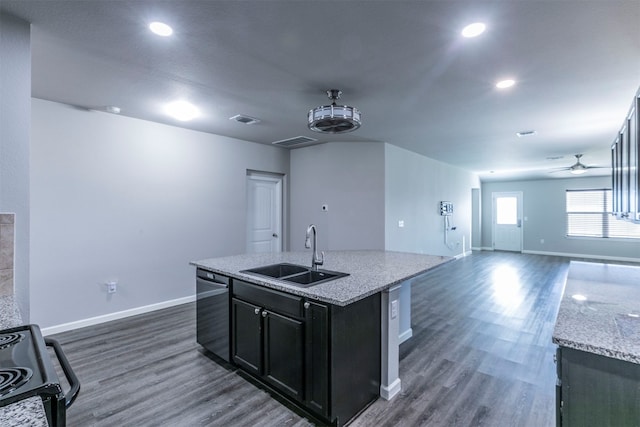 kitchen with sink, range, dark hardwood / wood-style flooring, light stone counters, and a center island with sink