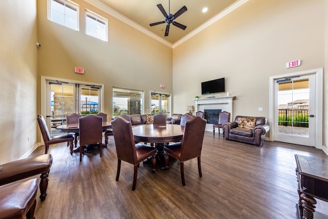 dining room with crown molding, dark hardwood / wood-style flooring, a tile fireplace, ceiling fan, and a high ceiling