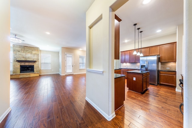 kitchen featuring dark wood-type flooring, stainless steel refrigerator with ice dispenser, a center island, pendant lighting, and decorative backsplash