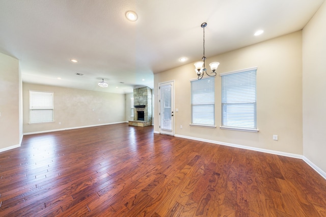 unfurnished living room featuring dark wood-type flooring, a fireplace, and an inviting chandelier