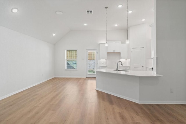 kitchen featuring high vaulted ceiling, white cabinetry, sink, hanging light fixtures, and light hardwood / wood-style flooring