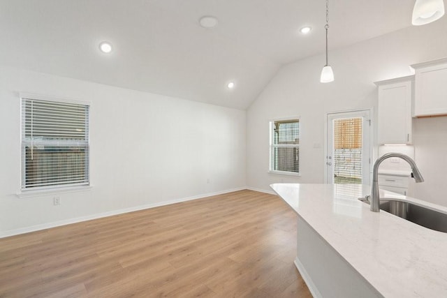 kitchen with lofted ceiling, sink, hanging light fixtures, light stone countertops, and white cabinets