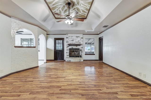 unfurnished living room featuring lofted ceiling, a stone fireplace, a tray ceiling, light wood-type flooring, and ceiling fan