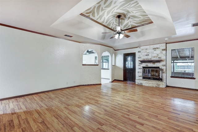 unfurnished living room with a tray ceiling, light wood-type flooring, a healthy amount of sunlight, and ceiling fan