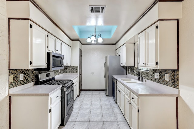 kitchen with appliances with stainless steel finishes, sink, a tray ceiling, pendant lighting, and white cabinets