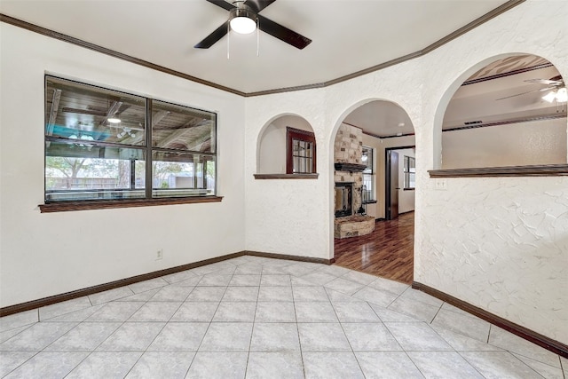 unfurnished room featuring light hardwood / wood-style floors, ornamental molding, a stone fireplace, and ceiling fan