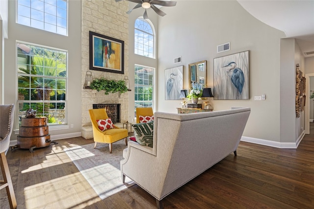 living room featuring a stone fireplace, dark hardwood / wood-style floors, and a towering ceiling